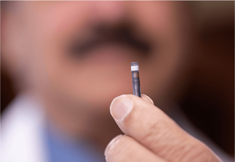 A close up of the small Eversense E3 sensor held between 2 fingers