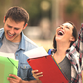 Two people celebrate, holding folders and papers, in an outdoor setting with blurred greenery in the background.